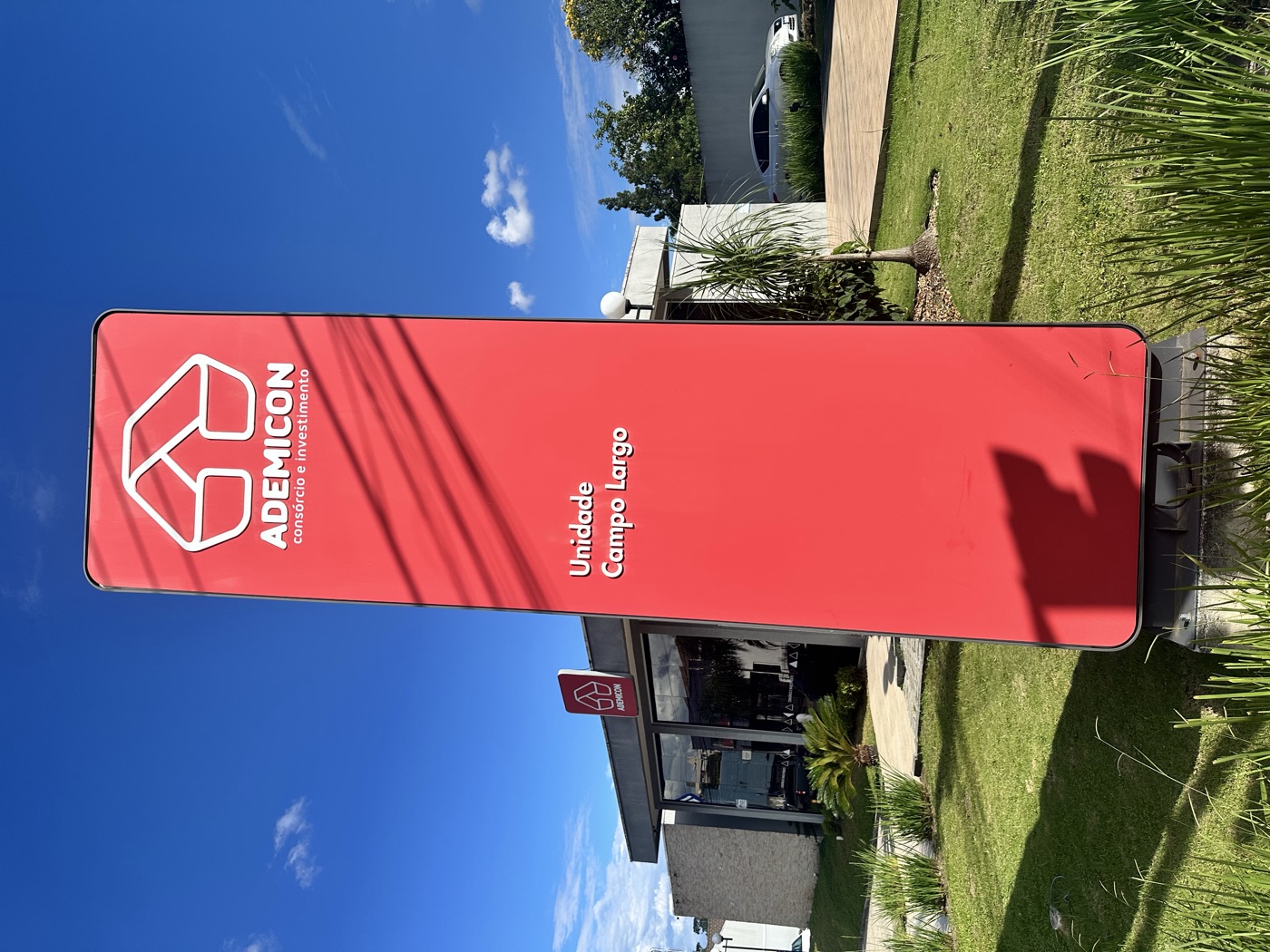Totem da Ademicon com a inscrição Unidade Campo Largo, e a unidade física ao fundo